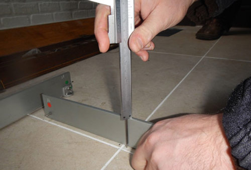 Het niveauverschil van twee naast elkaar geplaatste keramische tegels wordt gemeten met behulp van een rechte, stijve lat en een schuifmaat.